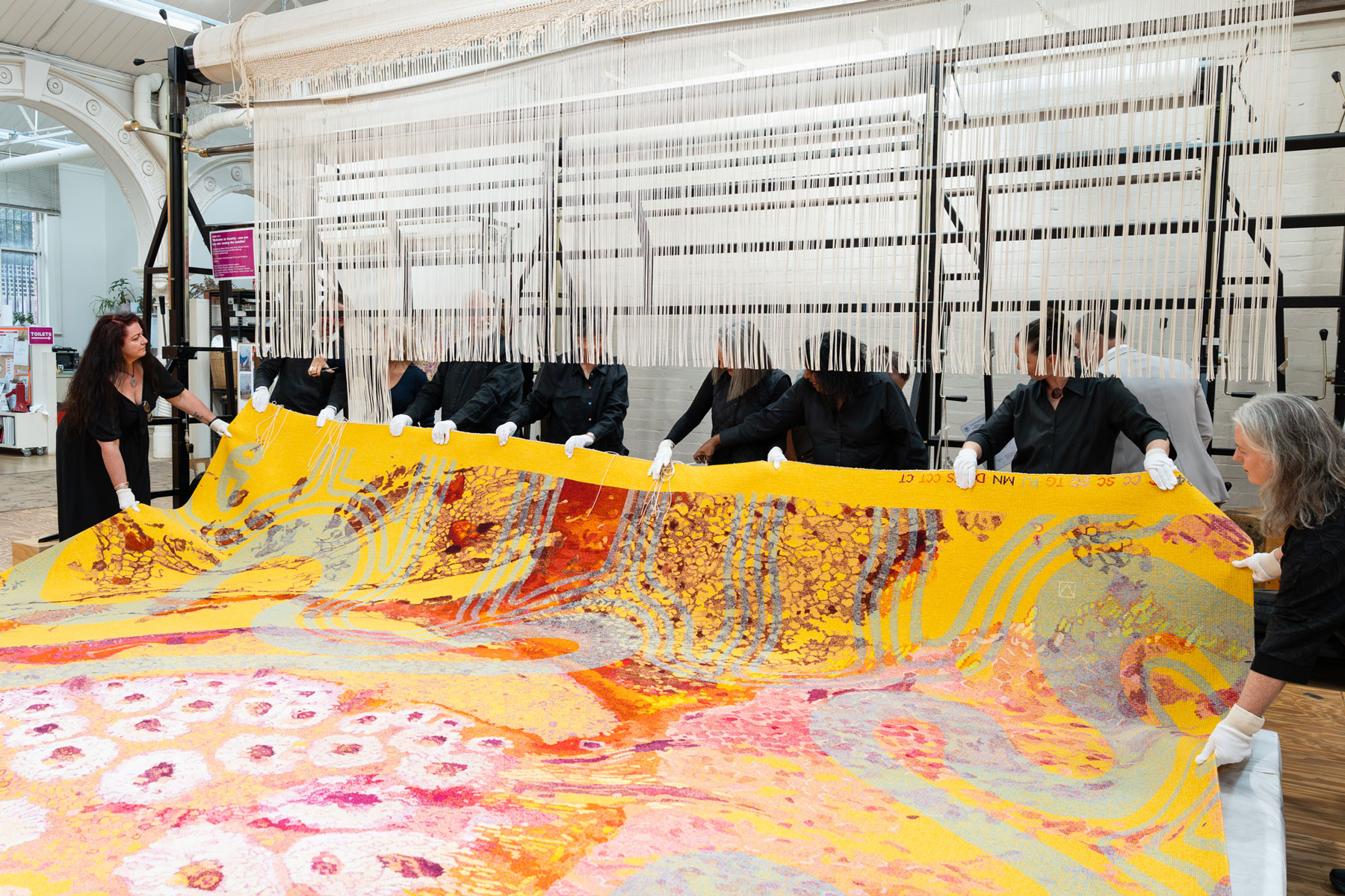 Cutting off ceremony for ‘Welcome to Country – now you see me: seeing the invisible’. Photo by Astrid Mulder. A large colourful tapestry is being cut of the loom
