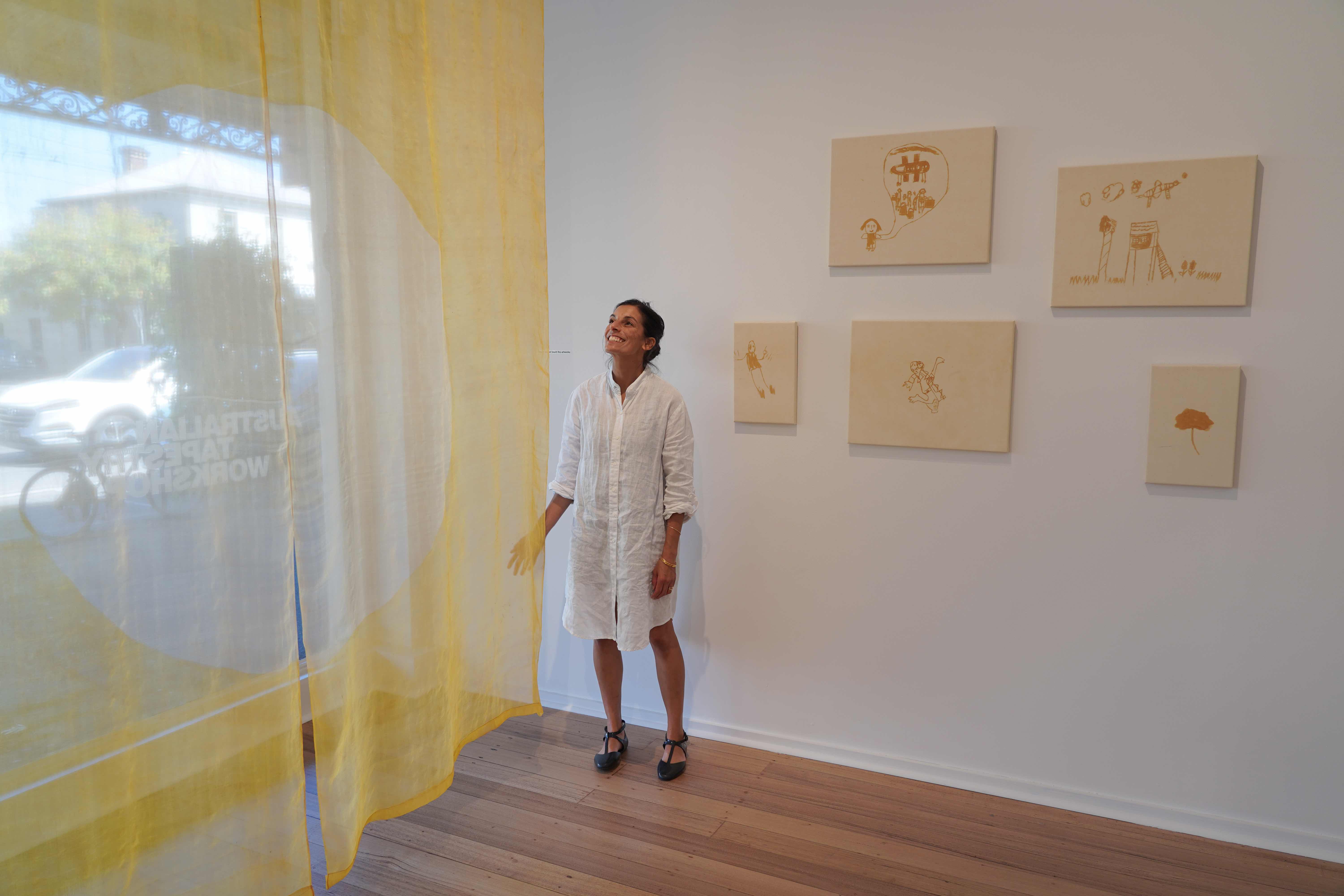 Sangeeta Sandrasegar in a gallery space surrounded by her artworks including draped cloth dyed yellow