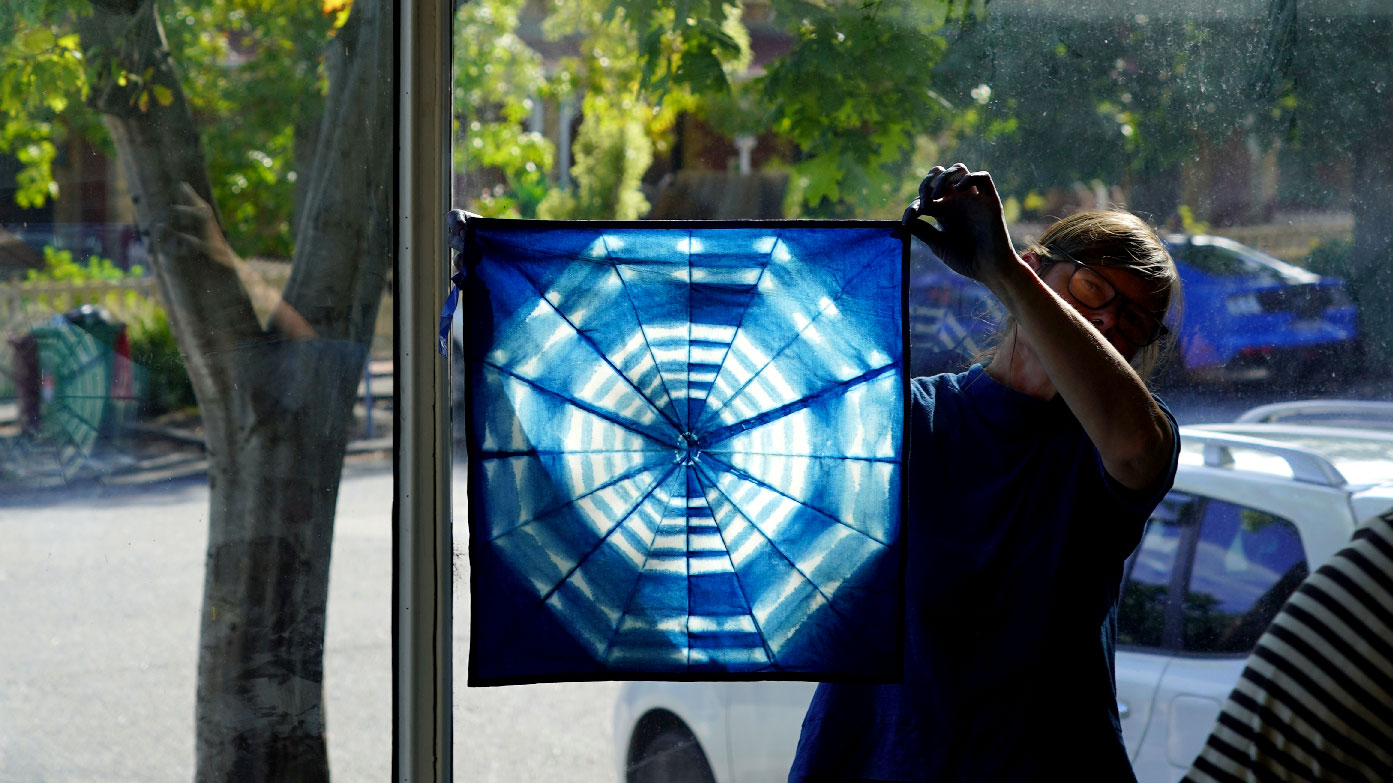 Heather standing in front of the window holding up a large swatch of indigo dyed fabric